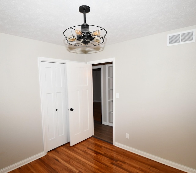 unfurnished bedroom featuring a textured ceiling, dark hardwood / wood-style flooring, and an inviting chandelier