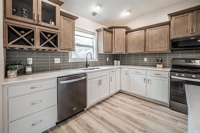 kitchen with lofted ceiling, decorative backsplash, white cabinetry, sink, and stainless steel appliances