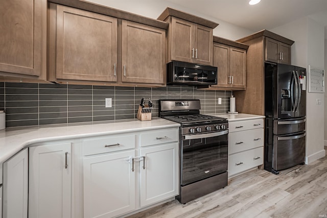 kitchen featuring white cabinetry, black appliances, light wood-type flooring, and decorative backsplash