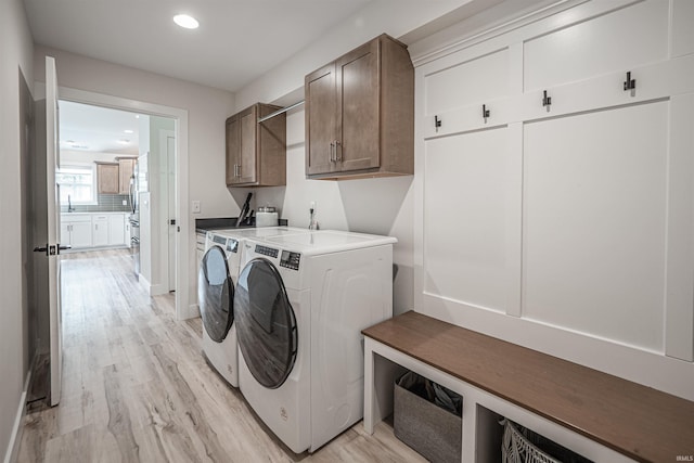 clothes washing area with light hardwood / wood-style flooring, washer and clothes dryer, and cabinets