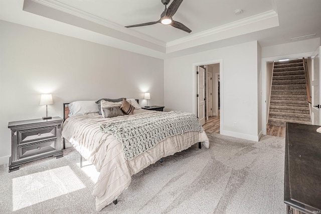 bedroom with ornamental molding, a tray ceiling, light colored carpet, and ceiling fan