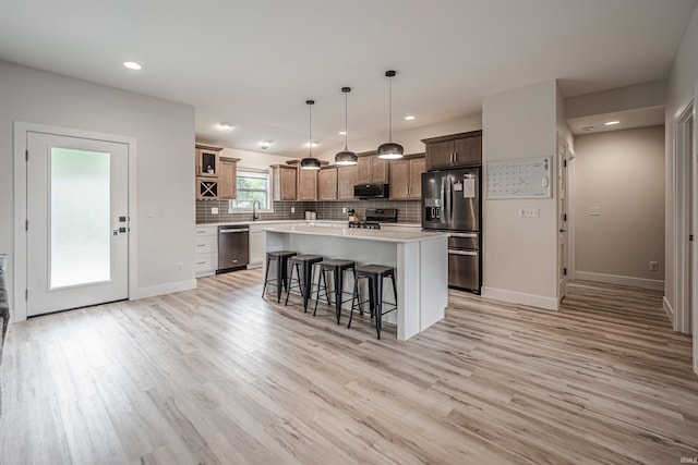 kitchen featuring appliances with stainless steel finishes, a kitchen bar, light wood-type flooring, pendant lighting, and a center island