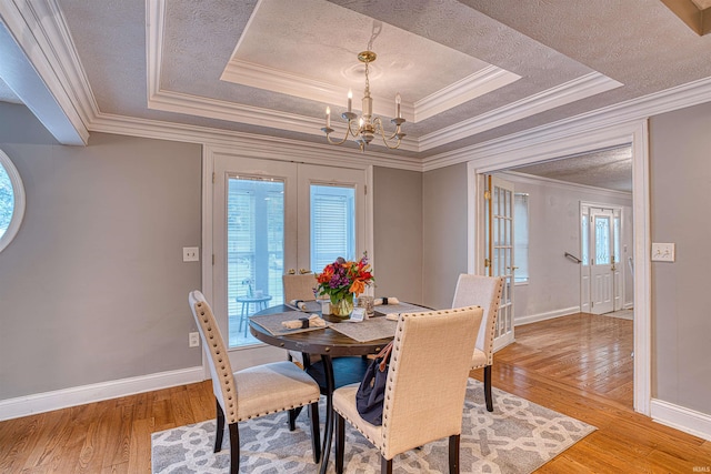 dining space with a raised ceiling, an inviting chandelier, light hardwood / wood-style flooring, crown molding, and french doors