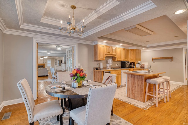 dining area featuring ornamental molding, a tray ceiling, and light wood-type flooring