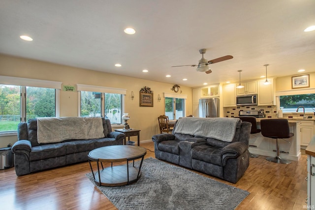 living room with ceiling fan, sink, and light wood-type flooring