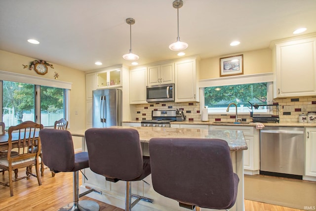 kitchen featuring hanging light fixtures, stainless steel appliances, white cabinets, light stone counters, and light hardwood / wood-style flooring