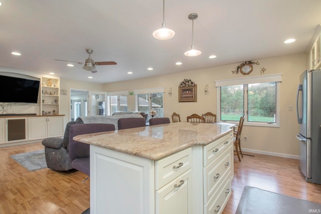 kitchen with light stone countertops, decorative light fixtures, light wood-type flooring, and stainless steel refrigerator