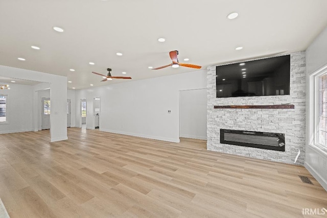 unfurnished living room with light hardwood / wood-style flooring, a stone fireplace, and ceiling fan