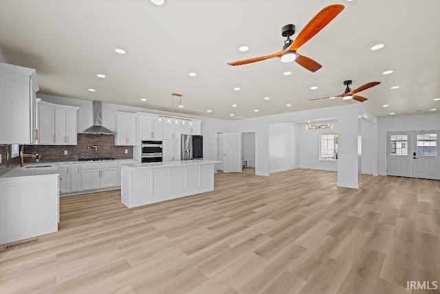 kitchen with wall chimney range hood, appliances with stainless steel finishes, light wood-type flooring, a center island, and white cabinetry