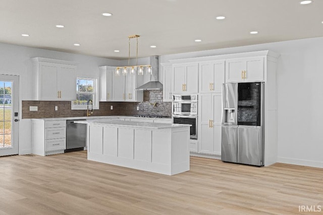 kitchen with wall chimney range hood, appliances with stainless steel finishes, decorative light fixtures, and white cabinets