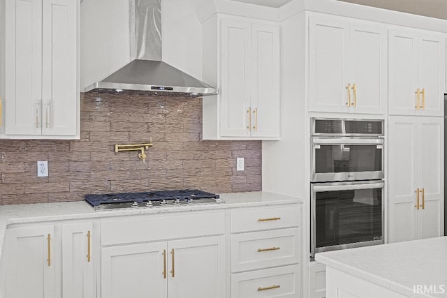 kitchen featuring decorative backsplash, wall chimney exhaust hood, white cabinets, and stainless steel appliances