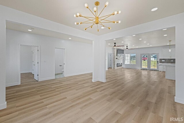 unfurnished living room featuring light hardwood / wood-style floors, a fireplace, and ceiling fan with notable chandelier