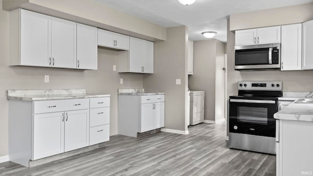 kitchen with sink, light stone countertops, white cabinets, light wood-type flooring, and appliances with stainless steel finishes