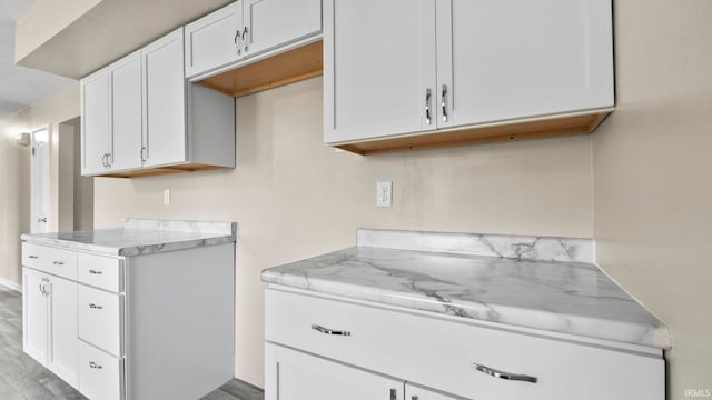 kitchen featuring light stone countertops, light wood-type flooring, and white cabinets