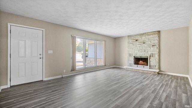 unfurnished living room featuring a baseboard radiator, hardwood / wood-style floors, a stone fireplace, and a textured ceiling