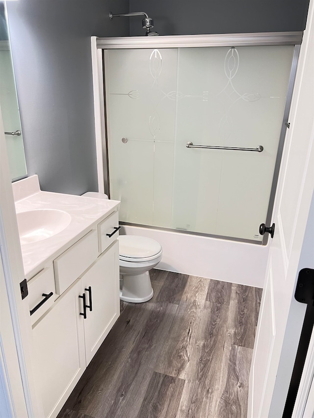 full bathroom with vanity, hardwood / wood-style floors, bath / shower combo with glass door, and toilet