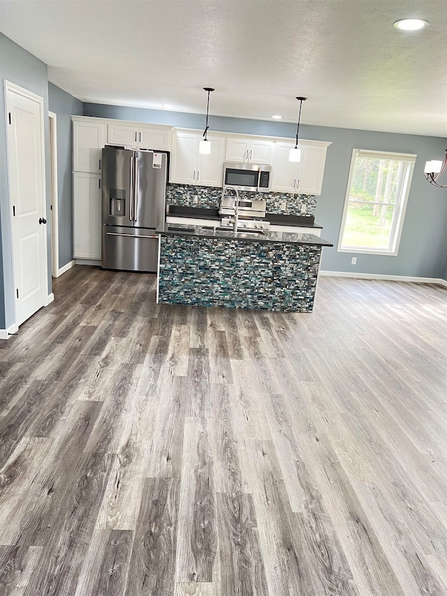 kitchen featuring white cabinets, hanging light fixtures, backsplash, appliances with stainless steel finishes, and hardwood / wood-style flooring