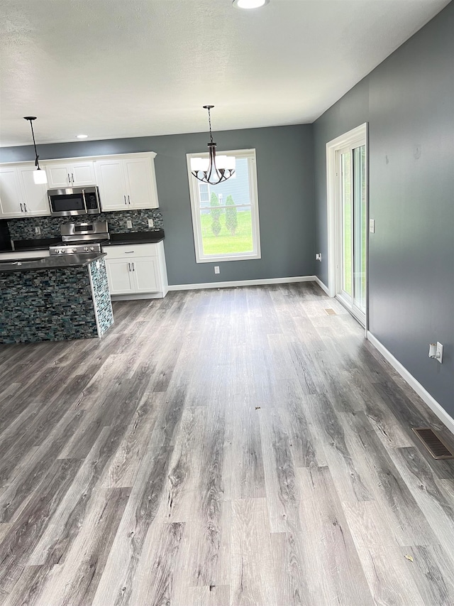 kitchen featuring appliances with stainless steel finishes, white cabinetry, hanging light fixtures, and a wealth of natural light