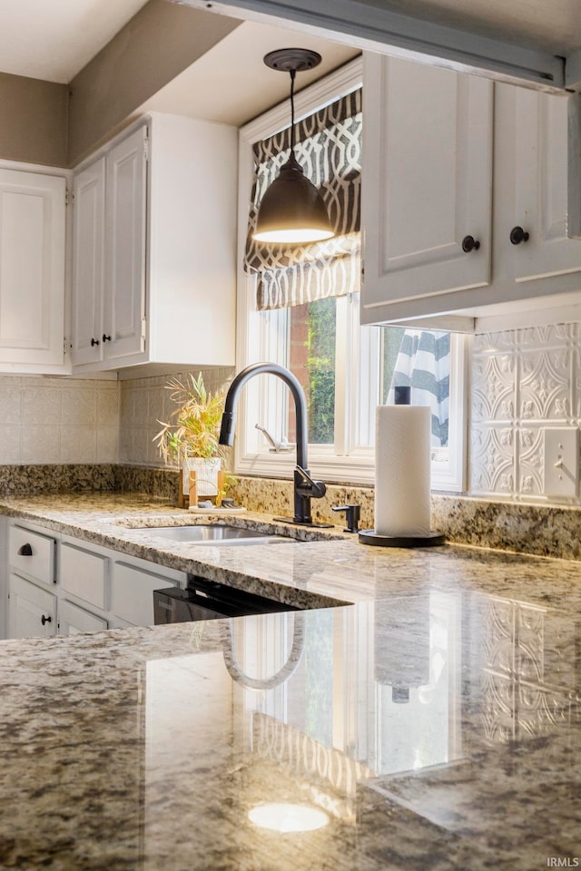 kitchen with tasteful backsplash, light stone countertops, sink, hanging light fixtures, and white cabinets