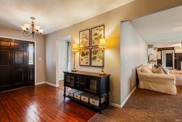 foyer entrance with dark wood-type flooring, a notable chandelier, and a textured ceiling