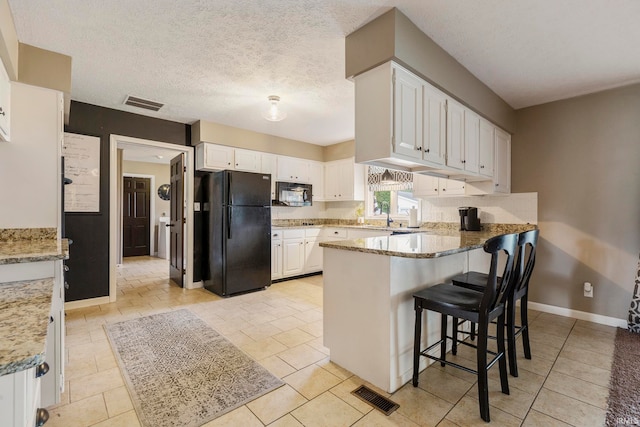 kitchen featuring black appliances, a kitchen bar, white cabinets, light stone counters, and a textured ceiling