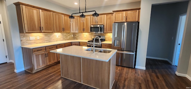 kitchen featuring decorative light fixtures, sink, stainless steel appliances, dark wood-type flooring, and a center island with sink