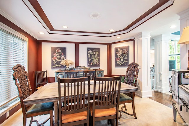 dining room with crown molding, decorative columns, a tray ceiling, and light hardwood / wood-style floors