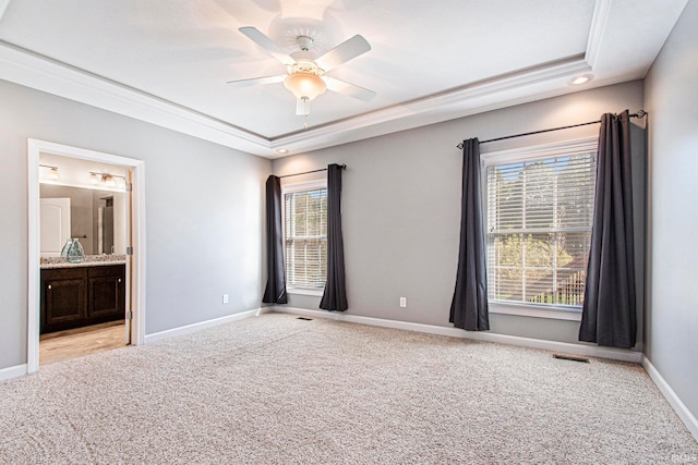 unfurnished bedroom with ensuite bathroom, a tray ceiling, light colored carpet, and ceiling fan