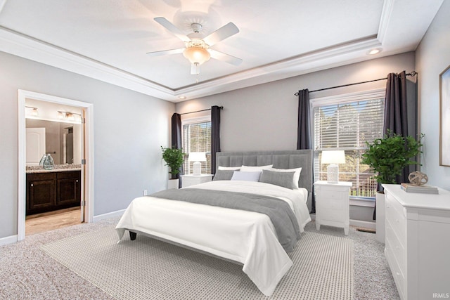 bedroom featuring light carpet, a tray ceiling, ensuite bath, crown molding, and ceiling fan