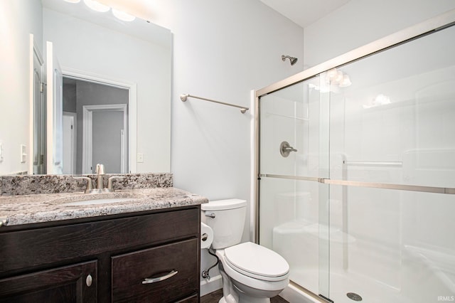 bathroom featuring a shower with door, vanity, and toilet