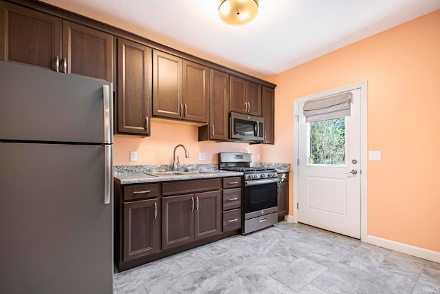 kitchen featuring dark brown cabinets, light stone countertops, stainless steel appliances, and sink