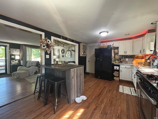 kitchen with sink, a kitchen breakfast bar, white cabinets, stainless steel gas range, and black refrigerator