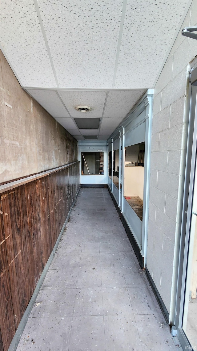 corridor with a paneled ceiling and wood walls