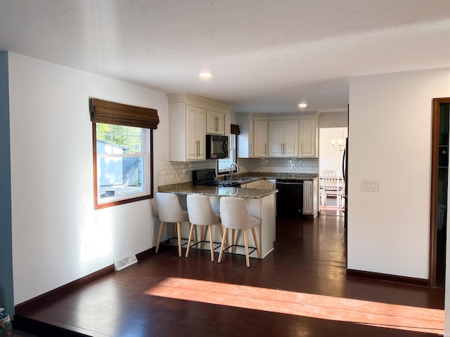 kitchen with a kitchen breakfast bar, kitchen peninsula, sink, black appliances, and tasteful backsplash