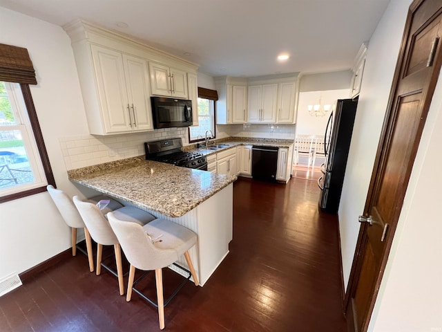 kitchen with kitchen peninsula, a breakfast bar, dark hardwood / wood-style floors, black appliances, and light stone counters