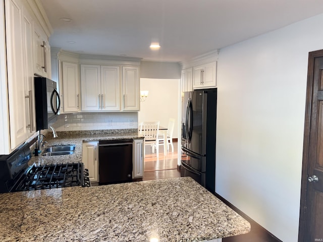 kitchen with light stone countertops, black appliances, wood-type flooring, white cabinets, and decorative backsplash