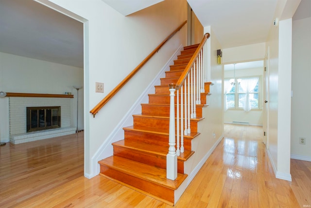 stairway with a brick fireplace and wood-type flooring