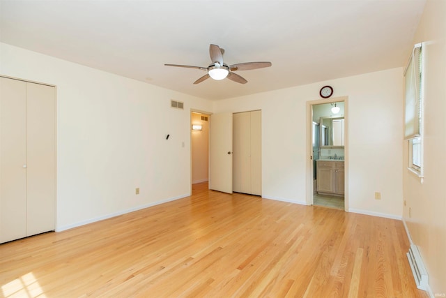 unfurnished bedroom with two closets, a baseboard radiator, ceiling fan, light hardwood / wood-style flooring, and ensuite bath