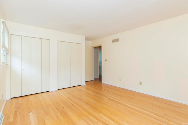 unfurnished bedroom featuring light hardwood / wood-style floors and two closets