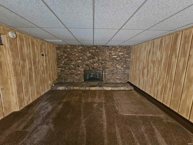 basement featuring carpet, a drop ceiling, and wooden walls