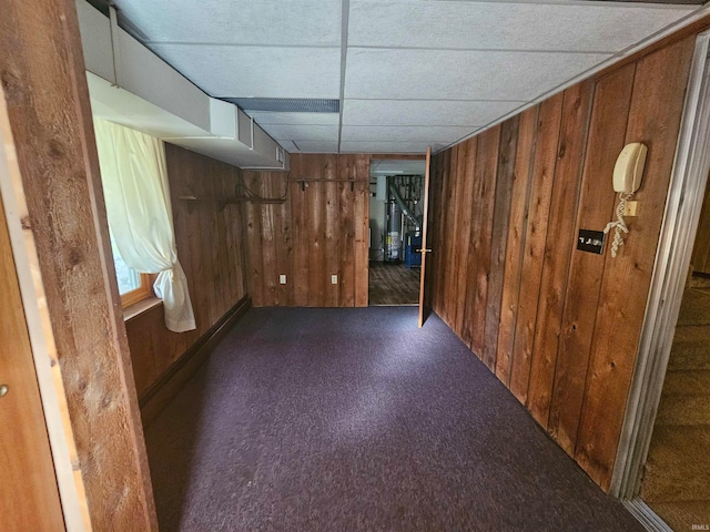 basement with wood walls, a paneled ceiling, and dark colored carpet