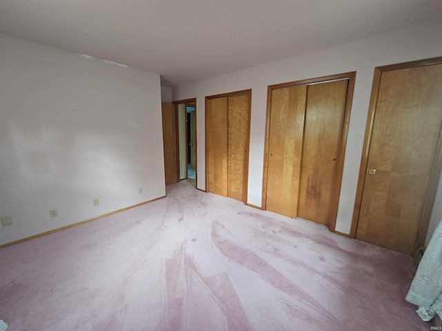 unfurnished bedroom featuring multiple closets and light colored carpet