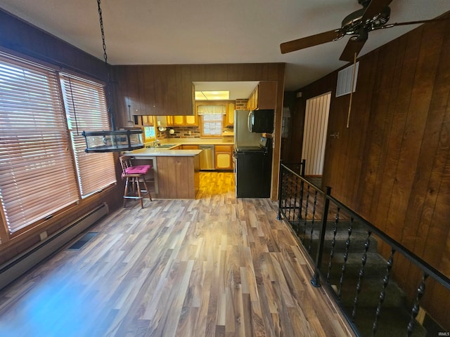 kitchen featuring dishwasher, wooden walls, kitchen peninsula, a kitchen bar, and light wood-type flooring