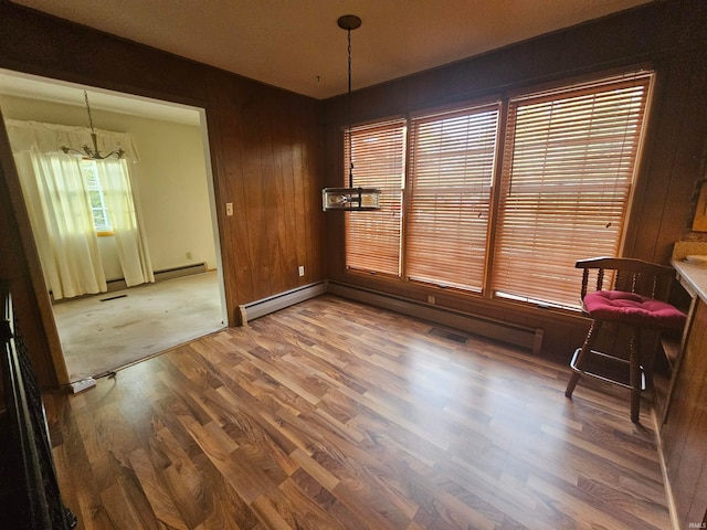 dining room featuring wooden walls, baseboard heating, wood-type flooring, and a chandelier