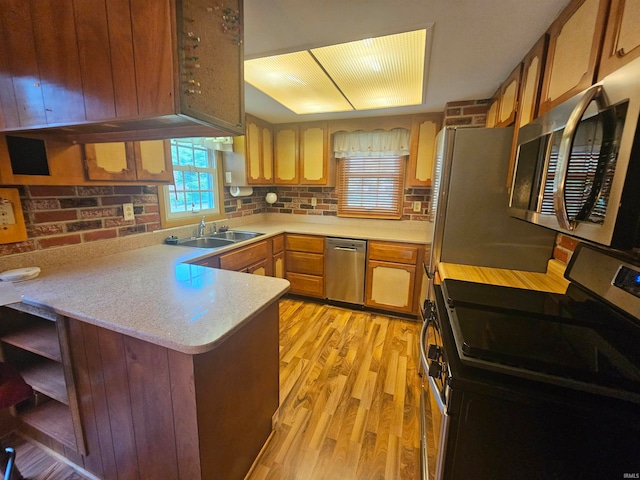 kitchen featuring kitchen peninsula, tasteful backsplash, appliances with stainless steel finishes, light wood-type flooring, and sink