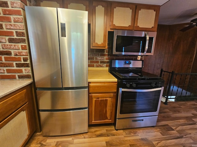 kitchen featuring brick wall, hardwood / wood-style floors, stainless steel appliances, and ceiling fan