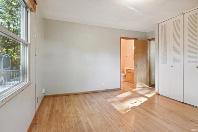 unfurnished bedroom featuring a closet, ensuite bathroom, and light wood-type flooring