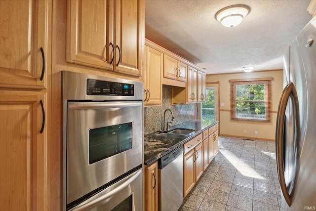 kitchen with sink, stainless steel appliances, dark stone countertops, decorative backsplash, and light brown cabinets