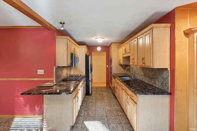 kitchen featuring light brown cabinets, backsplash, appliances with stainless steel finishes, dark stone countertops, and sink