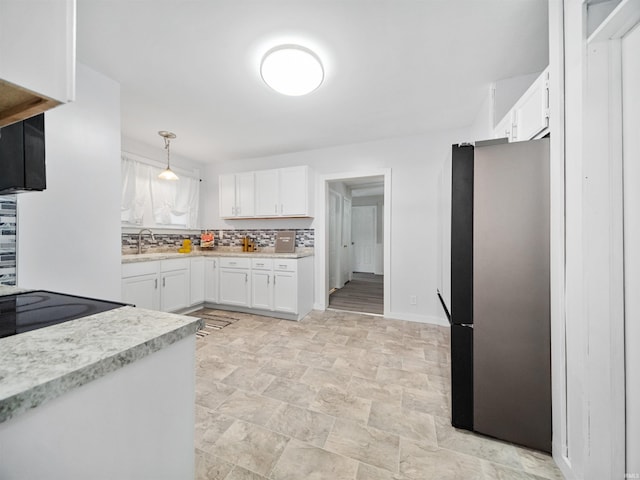 kitchen with decorative backsplash, stainless steel fridge, hanging light fixtures, white cabinetry, and sink